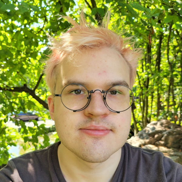 Picture of Daniel with pink hair and round glasses, against a tree/bush background